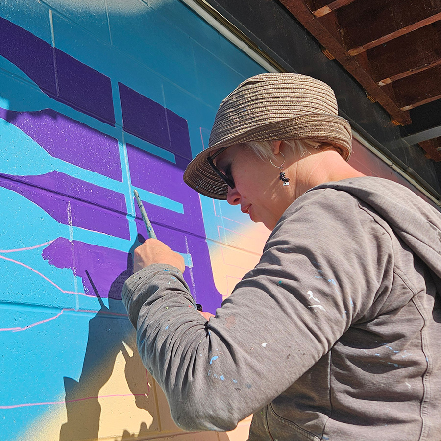 Margot painting a purple and blue geometric pattern on a cinder block wall