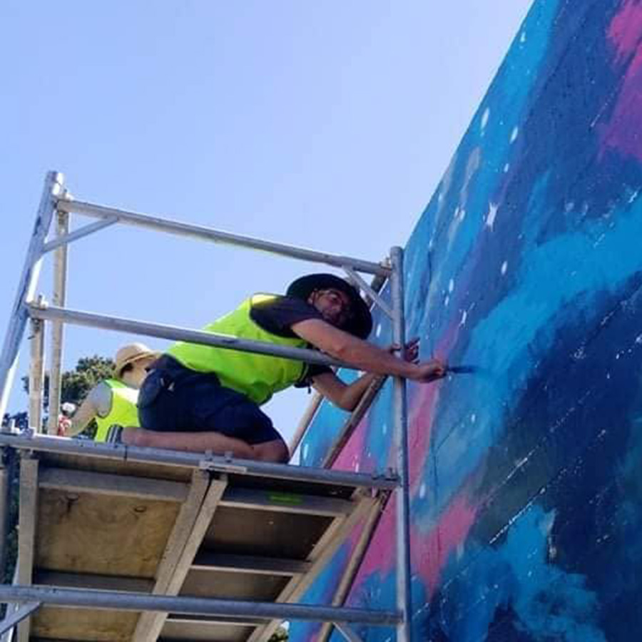 Nest Arts Collective members painting a blue and pink galaxy-style mural from scaffolding