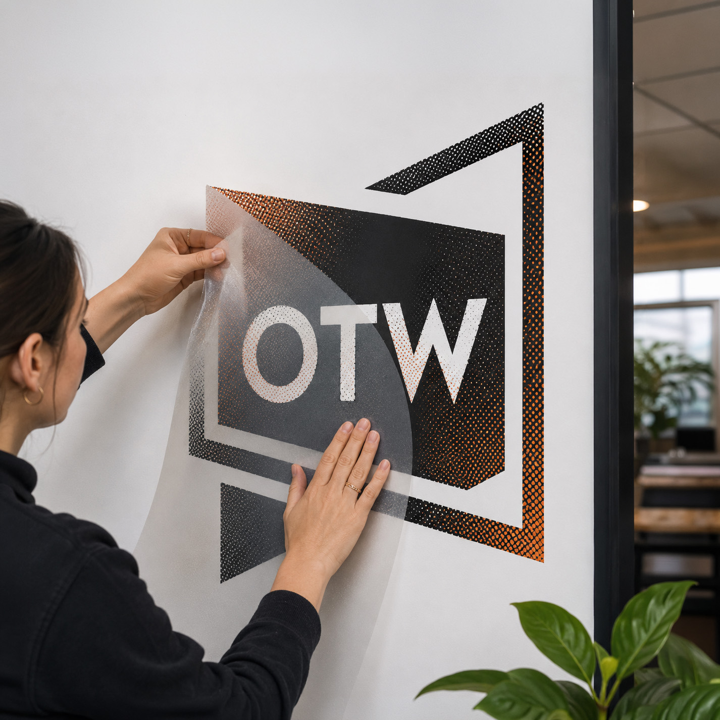 A person applying an OTW logo vinyl decal to a wall
