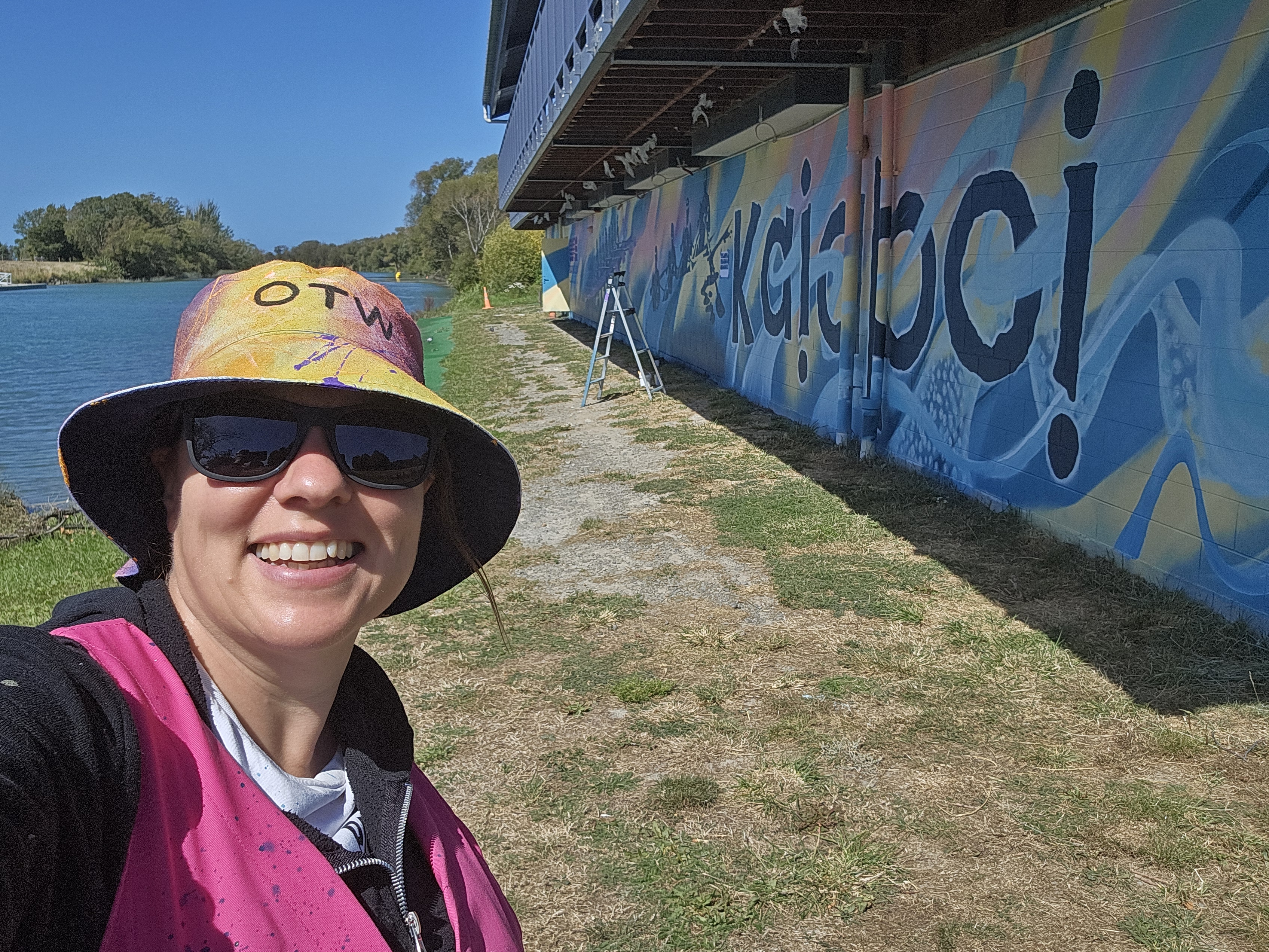 Mel Eaton in an OTW sunhat in front of the Pulling Together mural, the same person handling both design and painting