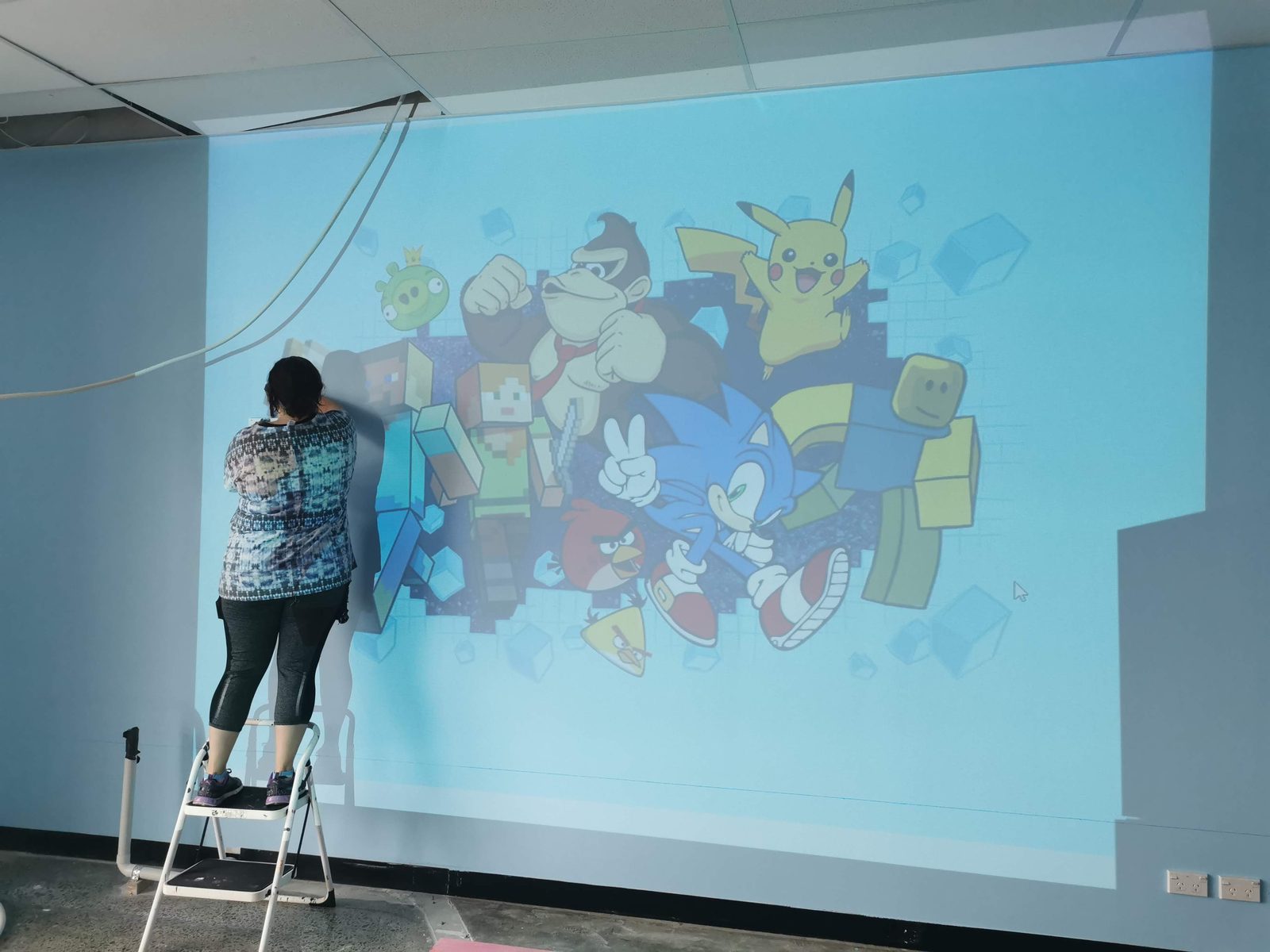 Pixel Party mural in progress — painting the character design from a scissor lift