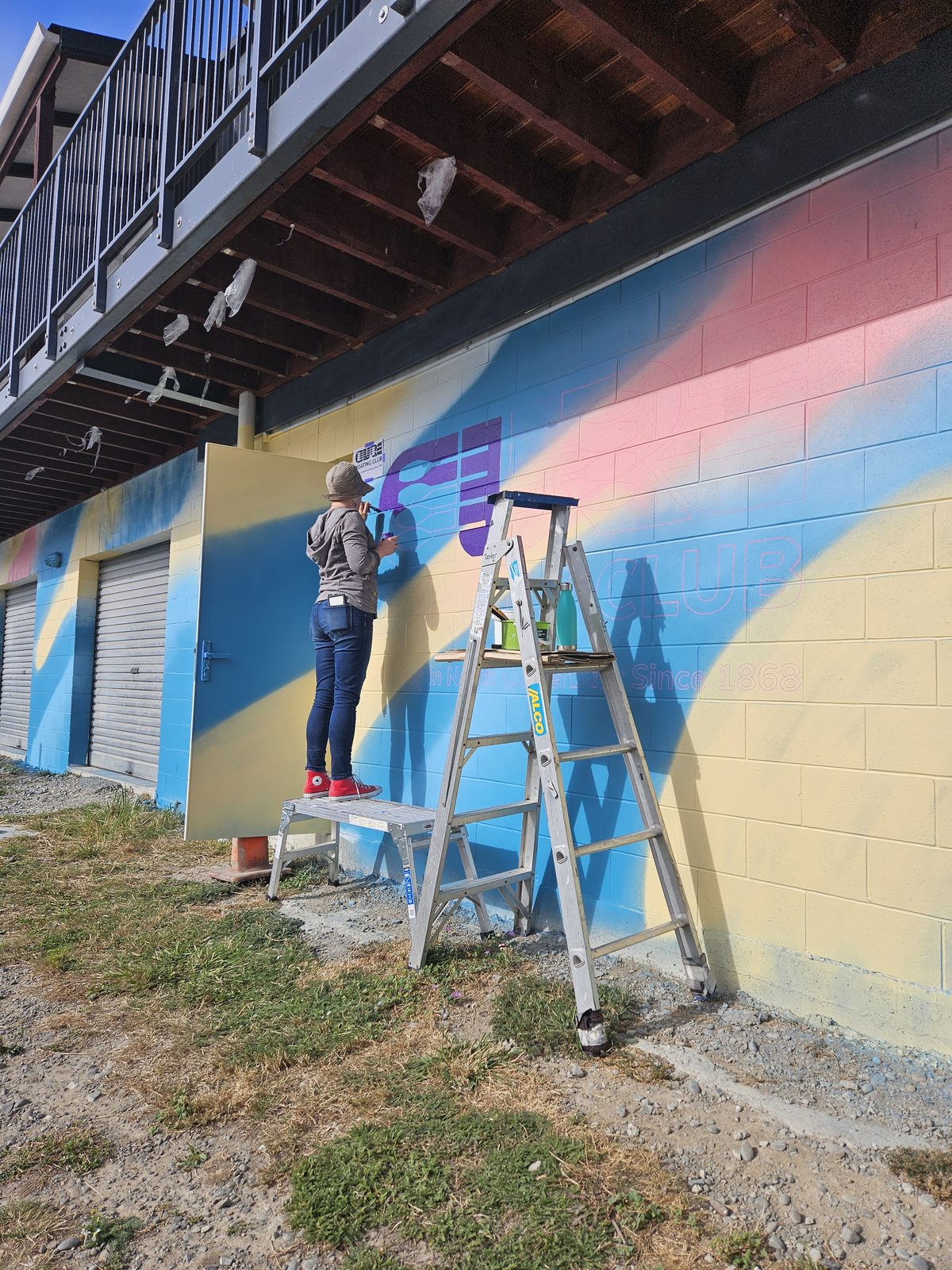Pulling Together mural in progress — painting the gradient background from a ladder