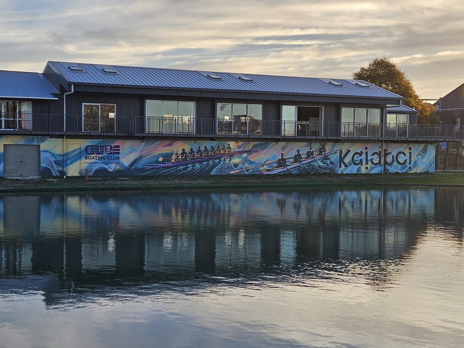 Pulling Together mural — long view of the clubrooms with the mural and river