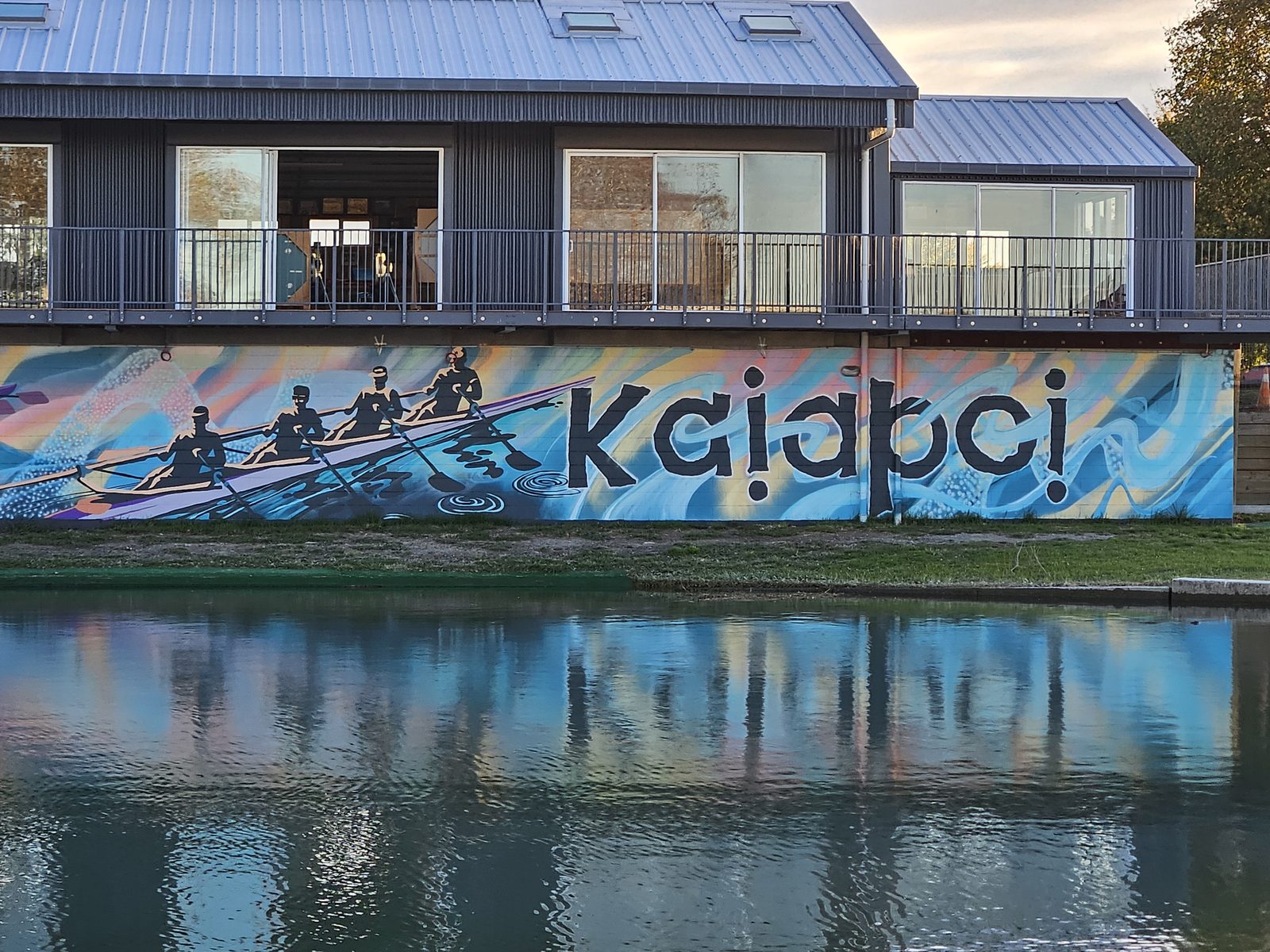 Pulling Together mural — 'Kaiapoi' lettering reflected in the still river water