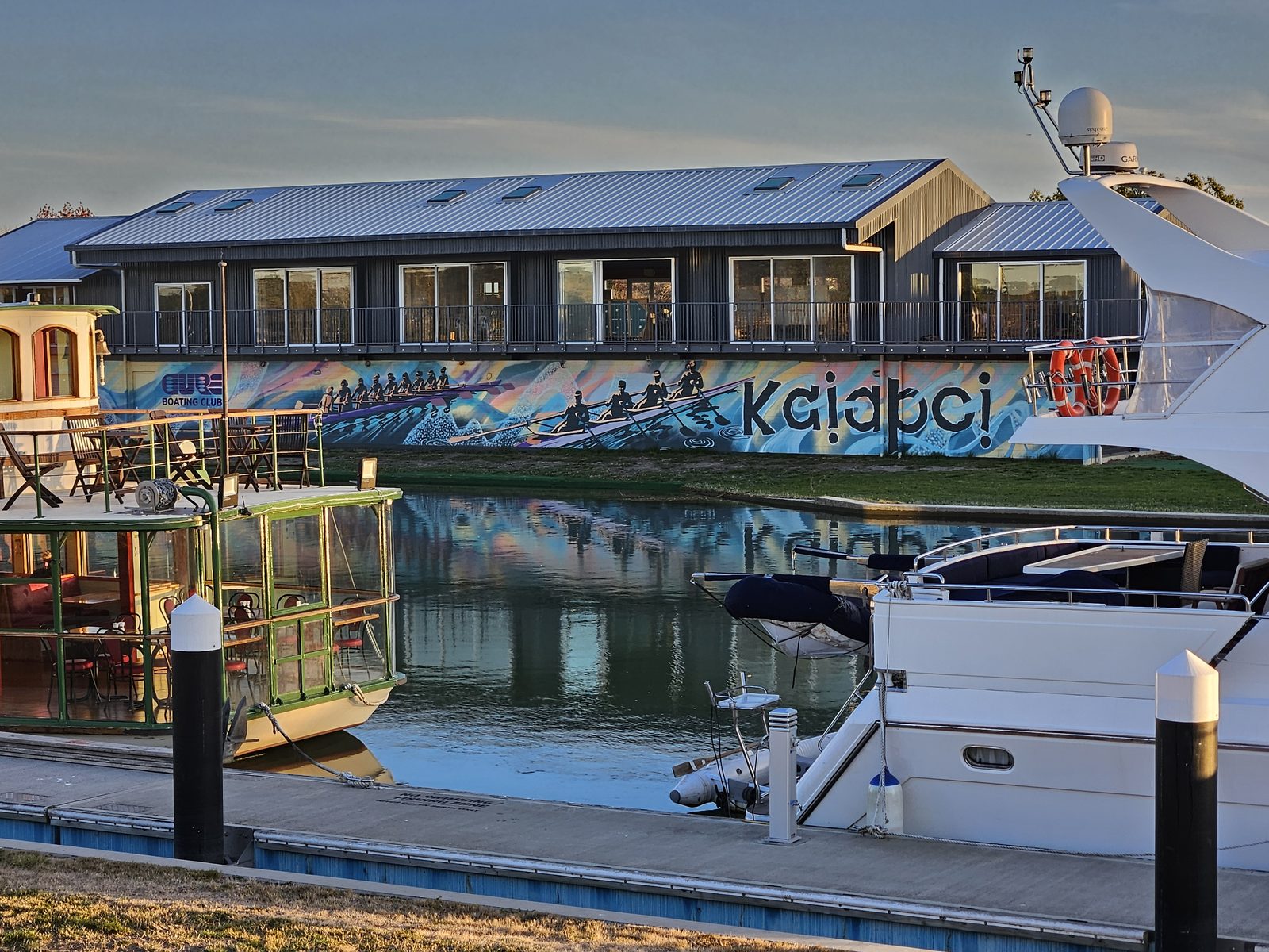 Pulling Together mural — boats moored near the painted clubrooms