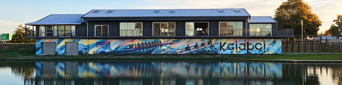 Pulling Together mural — full view of the rowers and 'Kaiapoi' lettering along the base of Cure Boat Club's riverside clubrooms