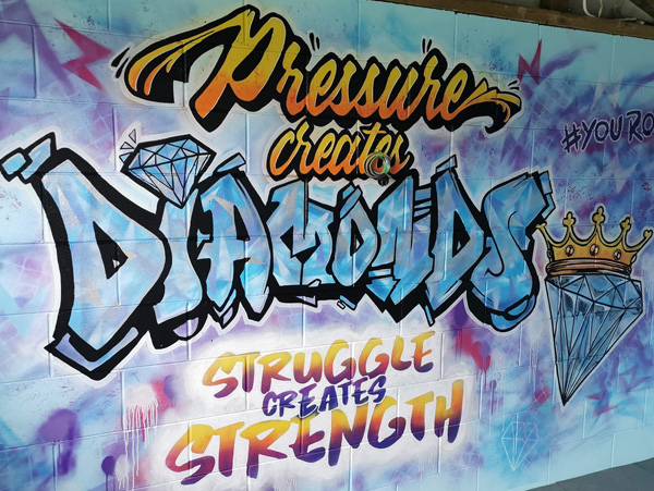 You Rock mural — graffiti-style lettering reading 'Pressure creates diamonds, struggle creates strength' with a diamond and crown graphic, Riddell Gym