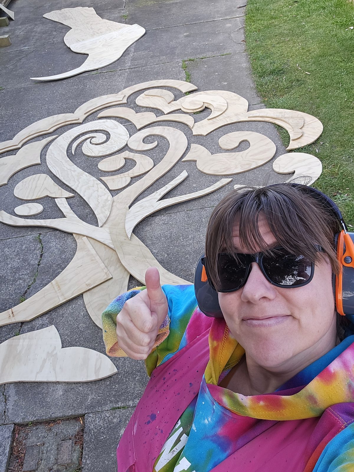 Around The Tree — Mel giving a thumbs up beside the koru pattern stencil on the ground