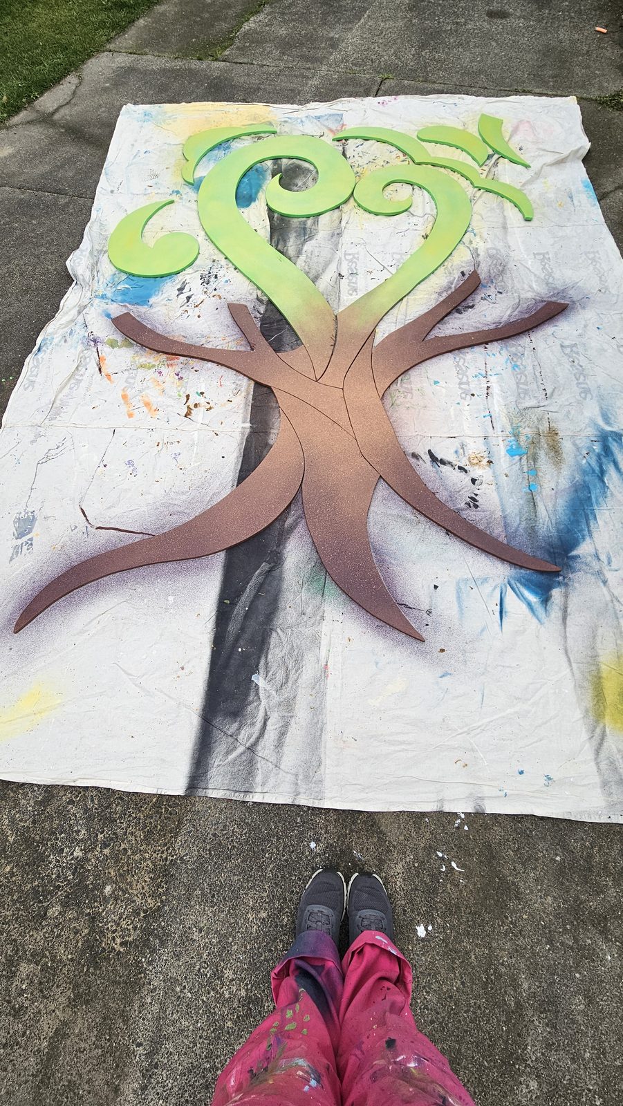 Around The Tree — a tree shape blocked in green on a ply panel laid flat for off-site painting
