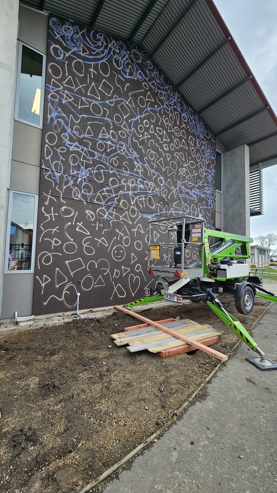 Around The Tree mural in progress — koru spiral pattern sketched onto the brown wall