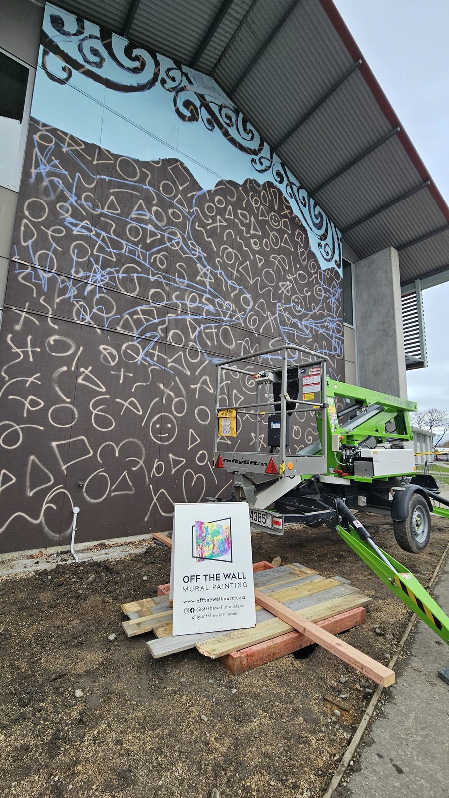 Around The Tree mural in progress — koru pattern outline with the lift positioned at the wall