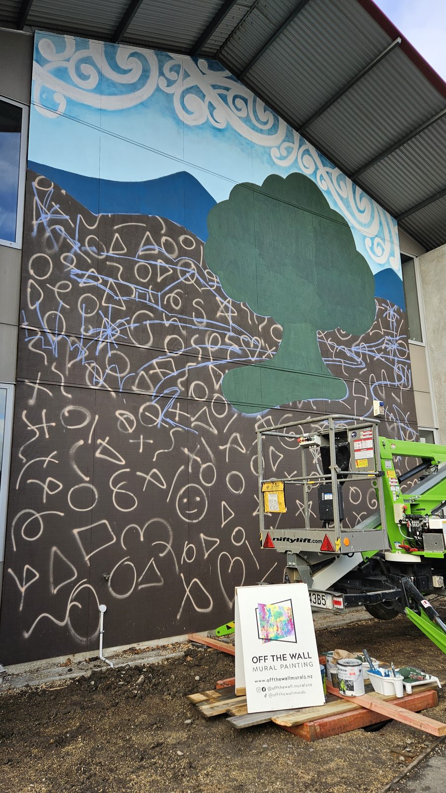 Around The Tree mural in progress — blue-green hills blocked in behind the koru outlines