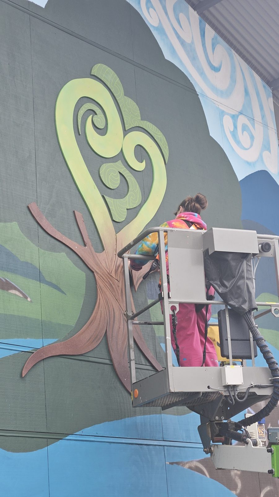 Around The Tree mural in progress — a koru-pattern tree painted green on a ply panel