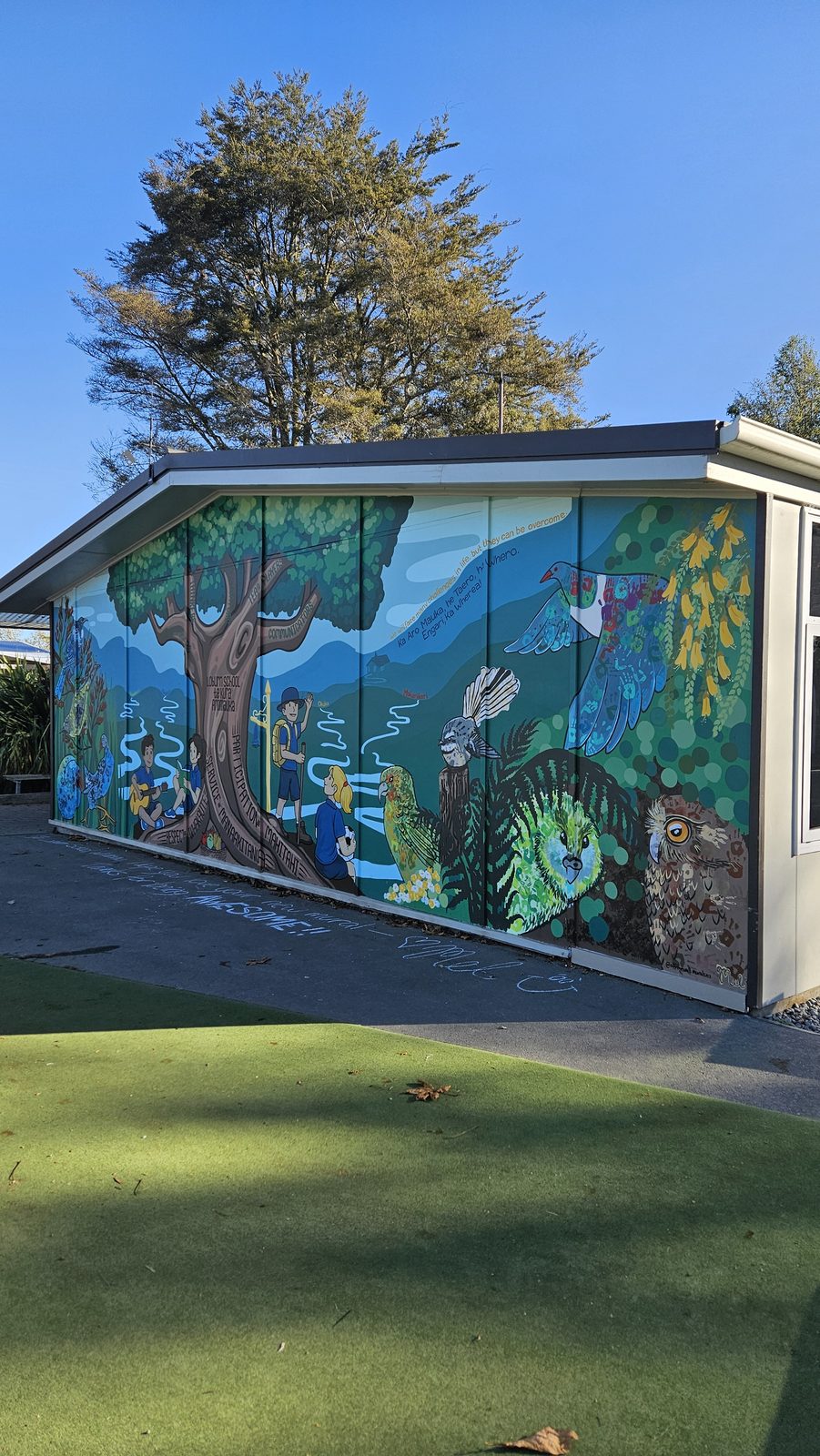 Flock Together — wide view of the school building and mural with trees and grass