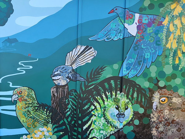 Flock Together mural — kererū, fantail, kea, kiwi and morepork native birds among ferns and kōwhai flowers, Loburn Primary School