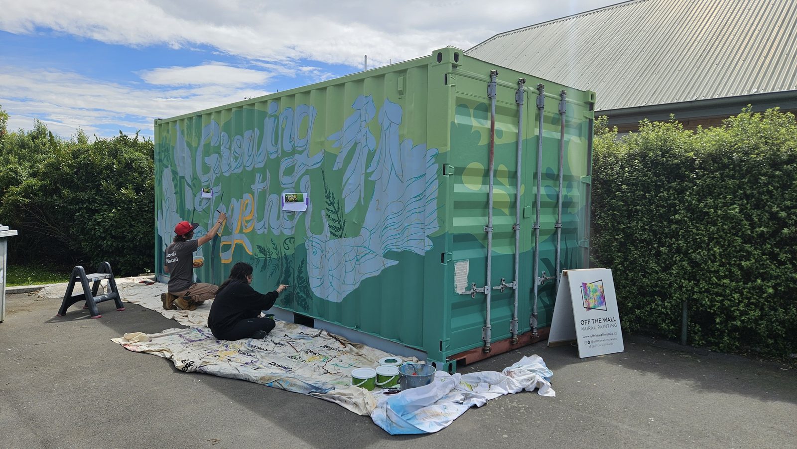 Growing Together mural in progress — Mel painting bird outlines at the base of the container