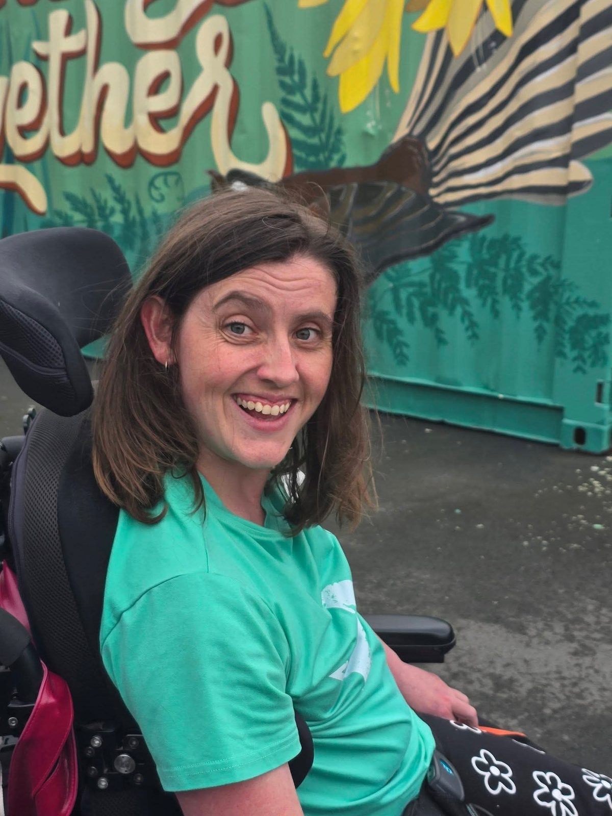 Growing Together — a Chris Ruth Centre resident in a wheelchair smiling in front of the mural