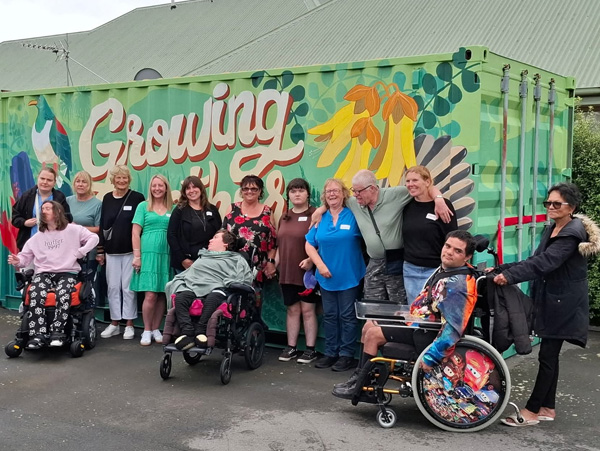 Growing Together mural — Chris Ruth Centre residents and staff in front of the painted shipping container with native bird and kōwhai motifs