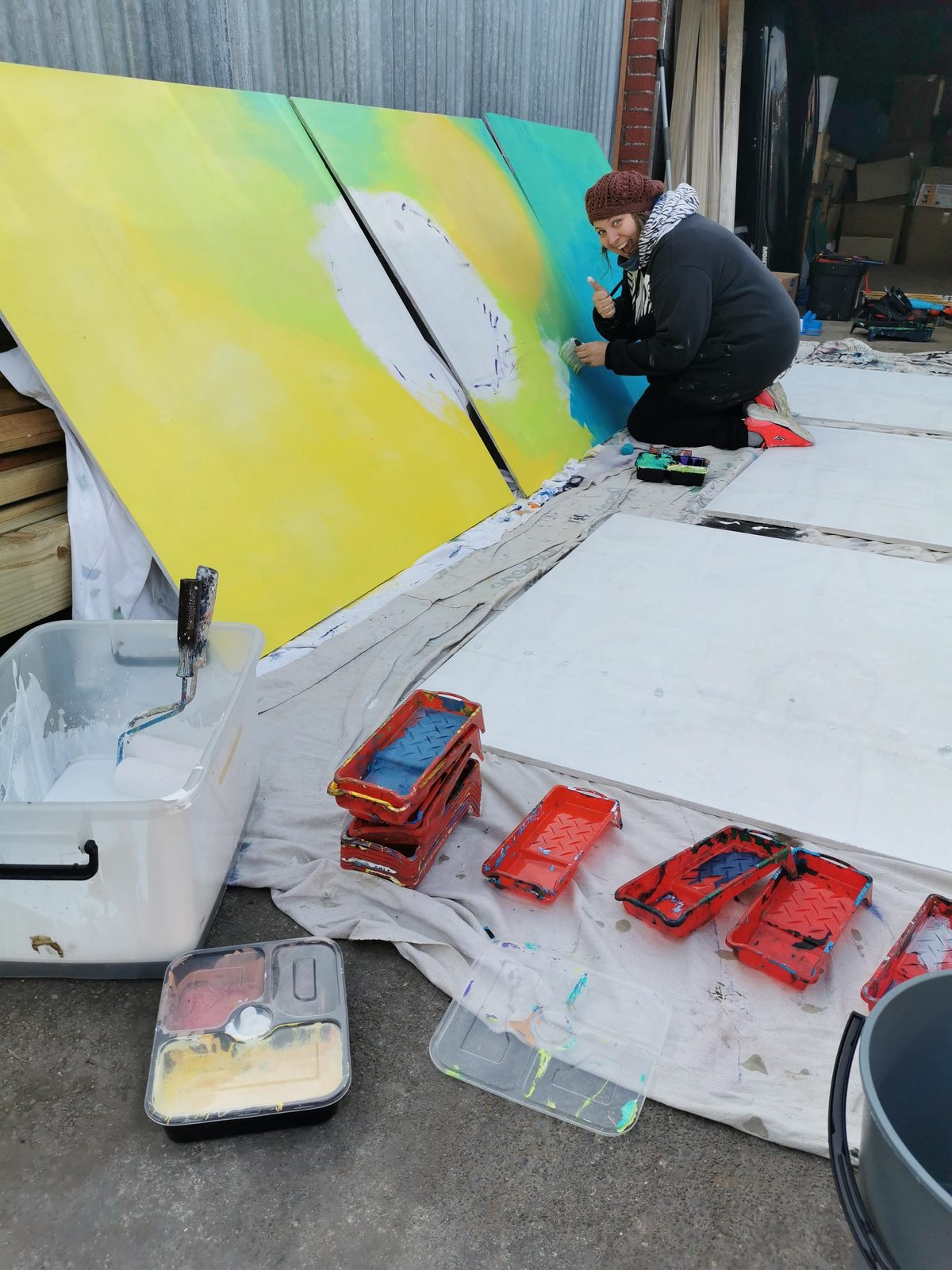 Natures Playground mural in progress — yellow and teal gradient background being painted on a panel