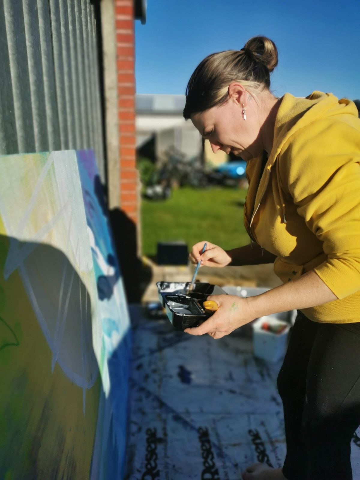 Natures Playground mural in progress — painting fine detail onto a panel against the workshop wall