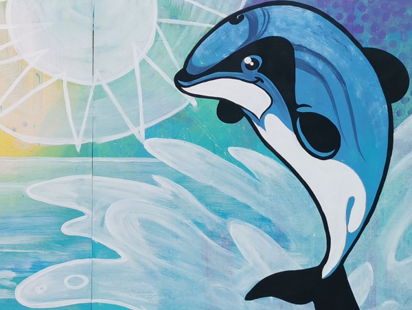 Natures Playground mural — a cartoon orca leaping from stylised waves under a sun, painted on the playground fence at Rangiora Play Centre