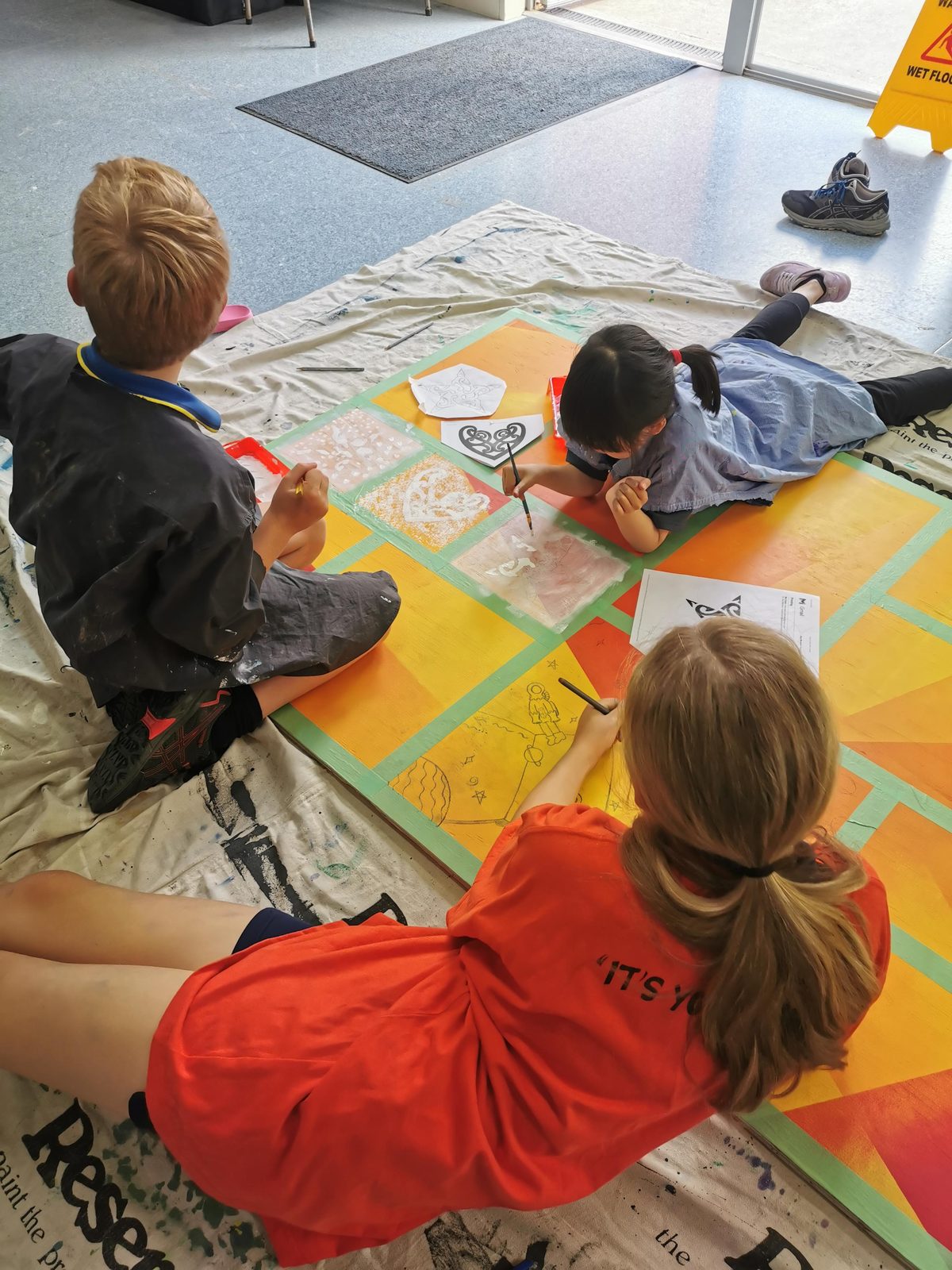Our Stars — students sitting on the floor working on a yellow and orange panel