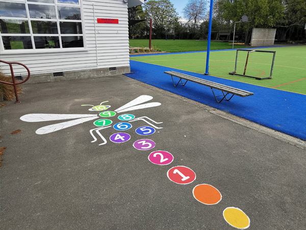 Playtime Bugs playground groundwork — a numbered hopscotch dragonfly game painted on the schoolyard asphalt, Cust Primary School