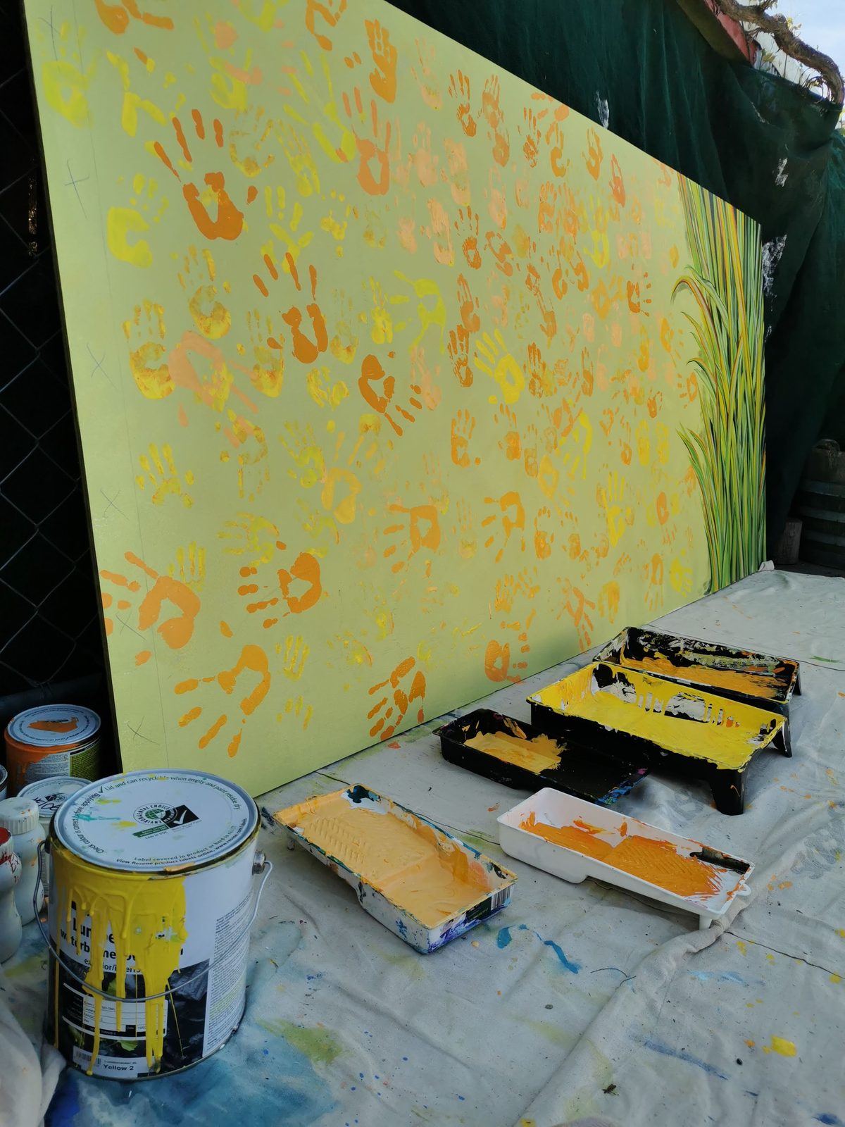 Weaving Together — a panel with orange and yellow handprints laid flat with paint supplies