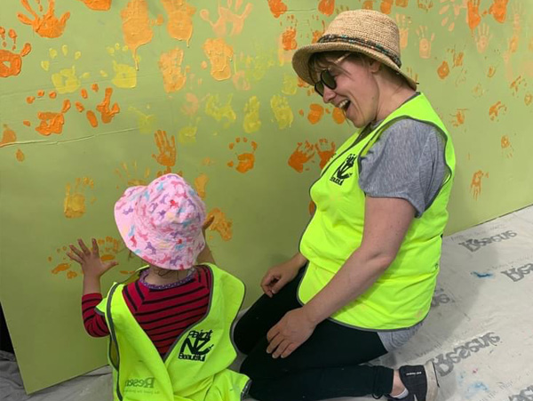 Weaving Together mural in progress — a parent and child adding handprints to the green background at Little Pepper Tree Preschool