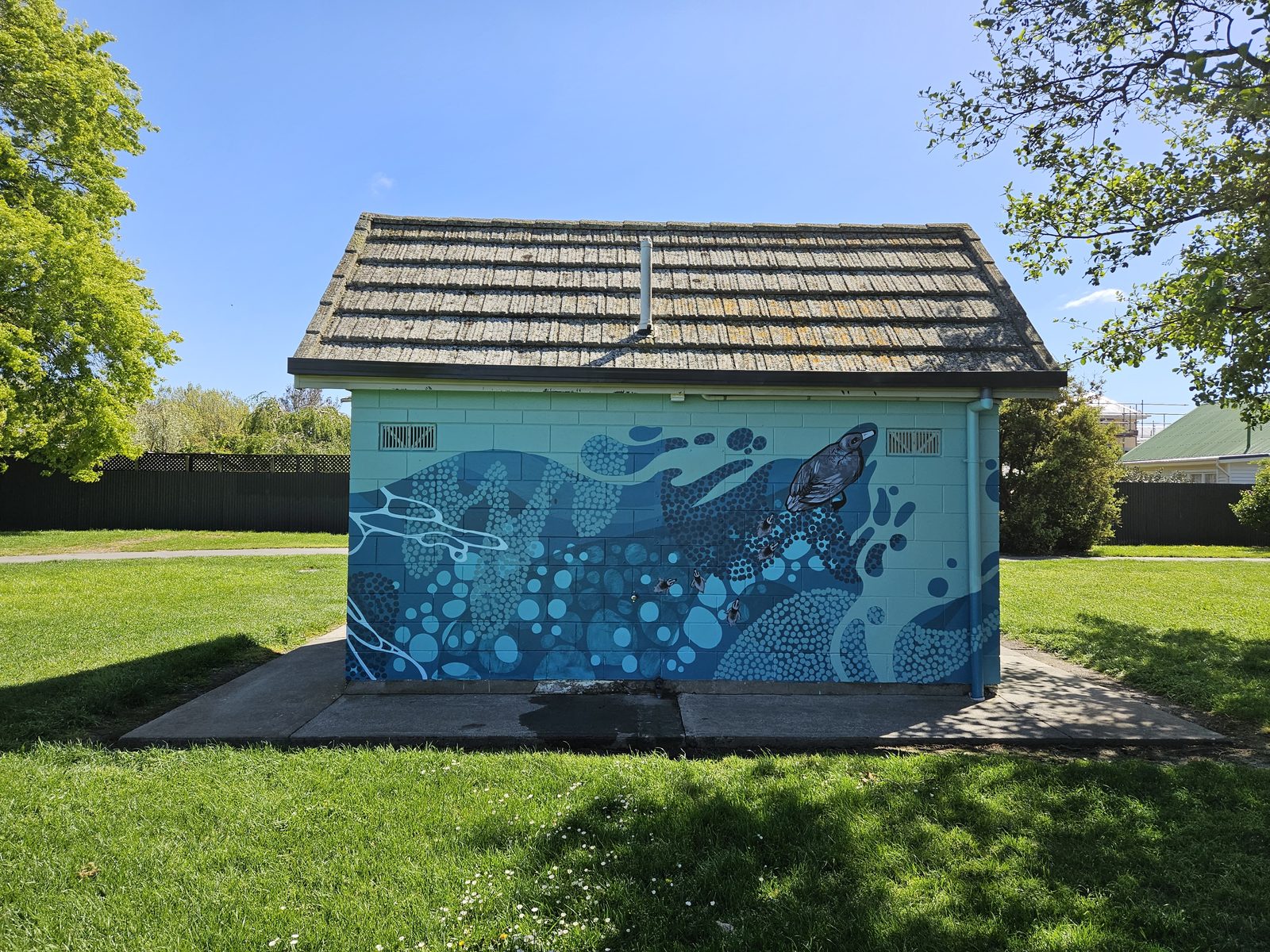 Flowing With Whio mural — finished toilet block exterior on a sunny day
