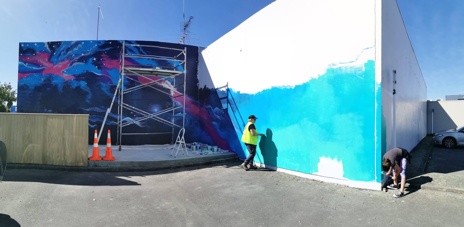 In Our Hands mural in progress — two painters blocking in the blue and white base design