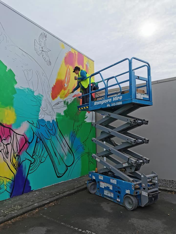In Our Hands mural in progress — painting the upper section of the wall from a scissor lift