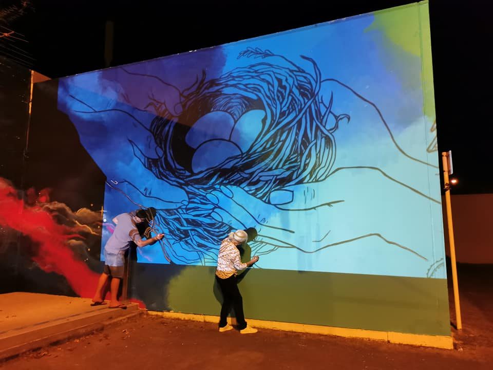 In Our Hands — two people viewing the finished mural at dusk under warm light