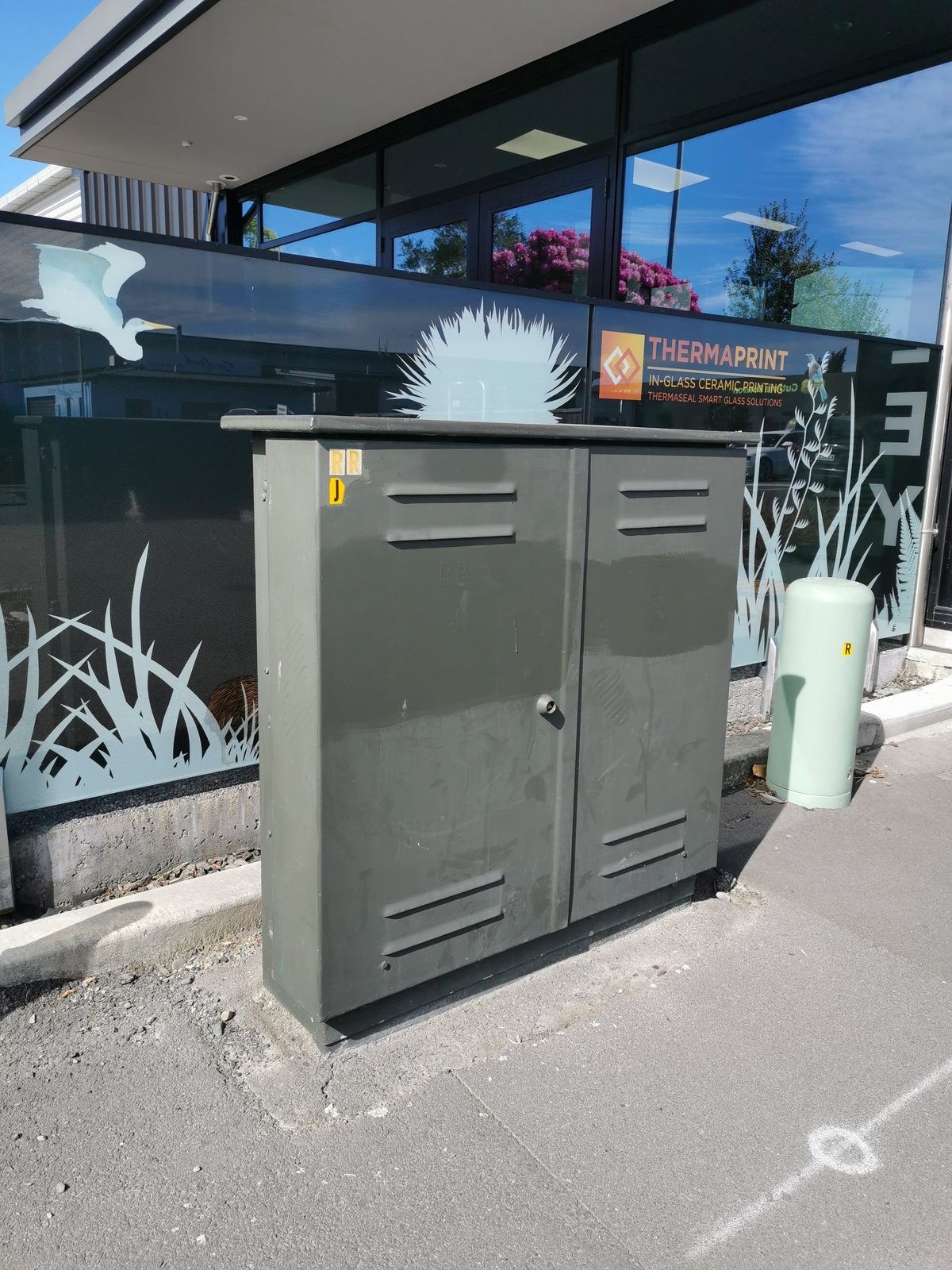Tui Song — plain grey Chorus cabinet before the mural, beside the silhouette grass decal wall