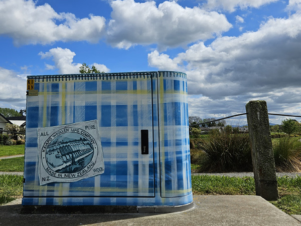 Woven History mural — blue and yellow tartan patchwork design with a Kaiapoi Woollen Mill label, painted on a Chorus street cabinet