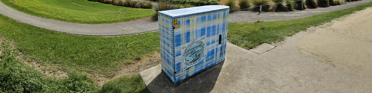 Woven History mural — full view of the blue and yellow tartan patchwork design on the Chorus street cabinet in a park setting